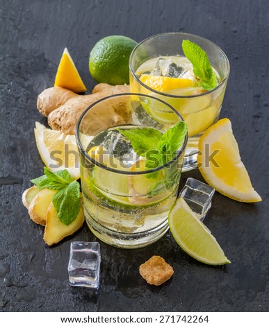 Ginger lemonade and ingredients - ginger, lemon, lime, mint, sugar, ice, dark stone background, water drops
