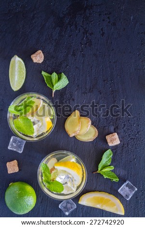 Ginger lemonade and ingredients - ginger, lemon, lime, mint, sugar, ice, dark stone background, top view
