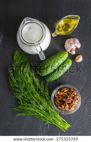 Tarator soup ingredients - yogurt, cucumber, dill, walnuts, garlic, oil, dark stone background, top view