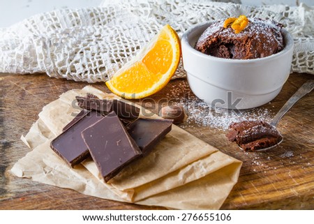 Chocolate orange muffin in white bowl, orange slice, nuts, chocolate, wood board, knitted napkin