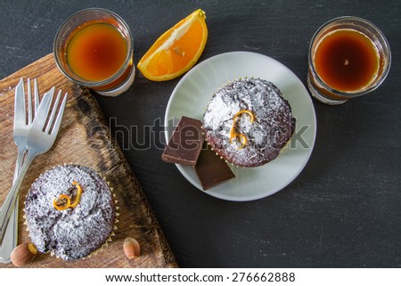 Chocolate and orange cupcakes, nuts, orange slice, chocolate, coffee maker, white plates, wood board, dark stone background, top view