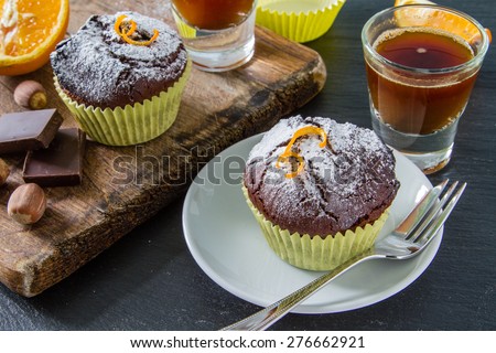 Chocolate and orange cupcakes, nuts, orange slice, chocolate, coffee maker, white plates, wood board, dark stone background