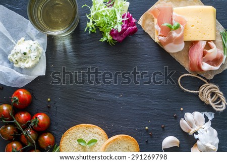 Sandwiches and ingredients - ham, cheese, salad, tomato, olives, wine, dark stone background, top view