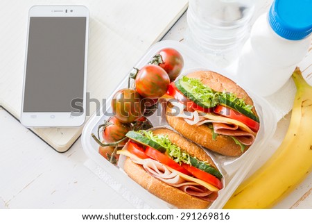 Lunch box - sandwiches, tomatoes, berries, cookies, milk, fruits, phone, notepad, white wood background
