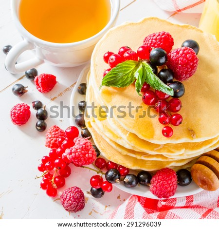 Pancakes with honey and berries, tea, juice, white wood background, top view
