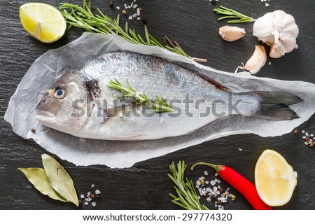 Raw fish with lemon, rosemary, salt, pepper, dark stone background, top view