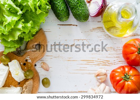Salad ingredients - lettuce, tomato, cucumber, onion, garlic, oil, feta, white wood background, top view