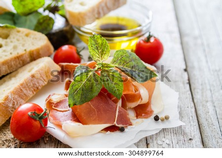 Appetizer - ham, bread, tomato, basil, oil, rustic wood background