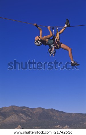 A climber dangles from her rope as she pulls her self across a tyrolean traverse.
