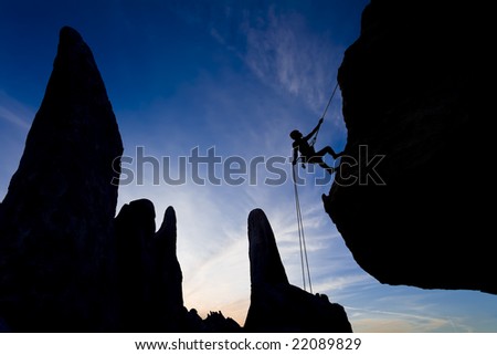 A climber rappelling from the summit of a rock spire is silhouetted against the evening sky, in The Sierra Nevada Mountains, California.