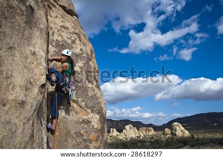 Female rock climber is focused on her next move as she battles her way up a steep cliff in Joshua Tree National Park, California.