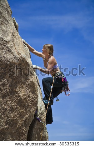 Female rock climber is focused on the next move as she battles her way up a steep cliff in Joshua Tree National Park, California.