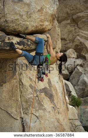 Clinging to an overhang a female climber is focused on her next move as she battles her way up a steep crack in Joshua Tree National Park, California.