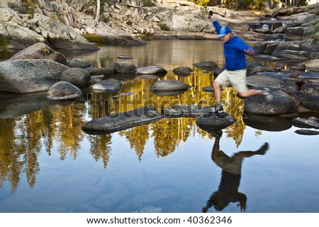 Hiker jumps from rock to rock as he crosses a river.
