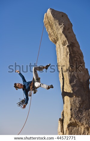 Climber in trouble dangling from her rope as she scales a rock pinnicle in the remote Mojave Desert of California.