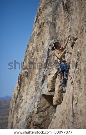 Female rock climber is focused on her next move as she battles her way up a steep cliff in Joshua Tree National Park, California.