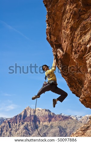Female rock climber  clings to an overhang in Red Rock Canyon on a sunny day.