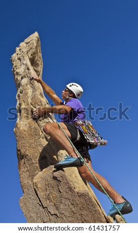 Male rock climber scrambles to the summit of a sheer pinnacle.