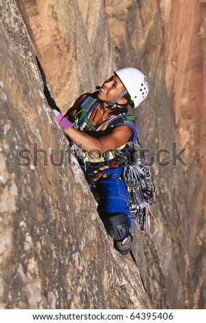 Female rock climber struggles for her next grip on the edge of a steep cliff.