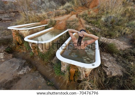 Young woman soaking in the rustic and funky Mystic Hot Springs,  the calcium rich water deposits create the organic textures flowing over the ground and into a recycled claw foot bathtub.