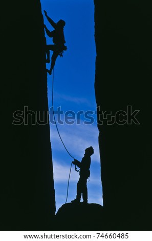 Team of rock climbers struggle to the summit of a steep cliff.