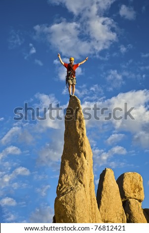 Rock climber balances on the summit of a steep spire after a successful ascent.