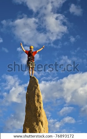 Rock climber balances on the summit of a steep spire after a successful ascent.