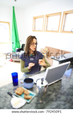 Woman working on her laptop and eating breakfast at home.