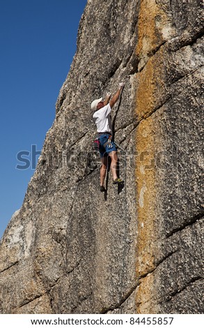 Male rock climber struggles for his next grip on a challenging, sheer cliff.