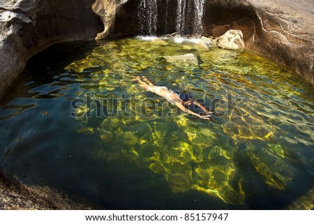 Woman swims underwater in a remote, prestine, natural pool.
