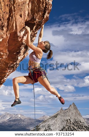 Female rock climber struggles to reach her next grip  on the edge of a challenging cliff.