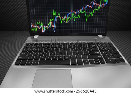 Stock chart on laptop computer monitor screen. Share price quotes of green and blue growth up trend on display over dark background. Modern technology internet live bank MORE SIMILAR IN MY GALLERY