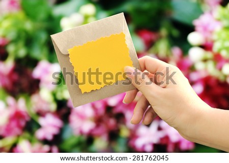 hand holding yellow card and brown envelope on blur  pink rangoon creeper background