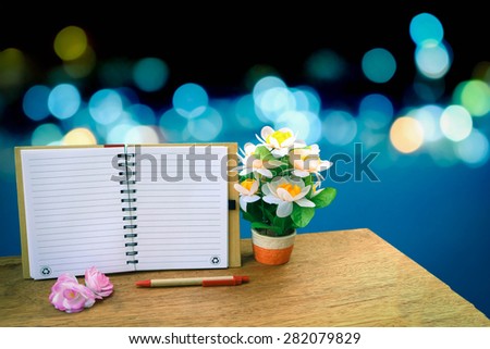 open notepad and flower vase on blur bokeh light in city backgrund