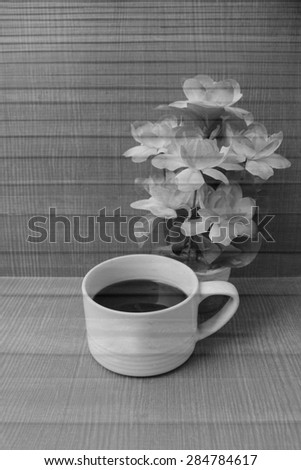 cup of black coffee and pink flower vase on wooden wall background in black and white tone