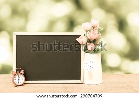 blackboard and watering pot vase on bokeh from tree background in vintage tone