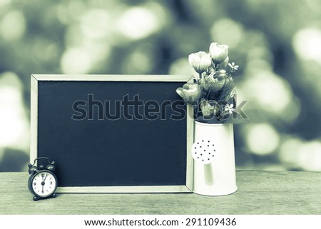 blackboard and watering pot vase on bokeh from tree background in green vintage tone
