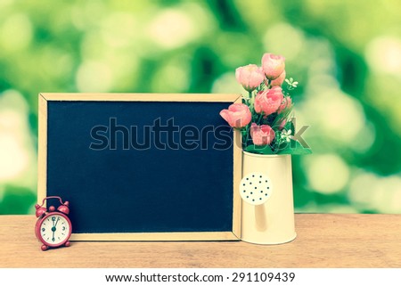 blackboard and watering pot vase on bokeh from tree background in vintage tone