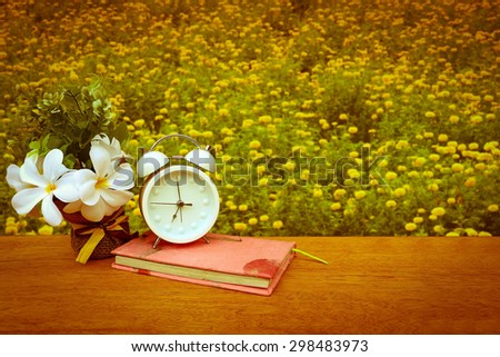 flower vase and clock on book with blur marigold garden background ,vintage tone