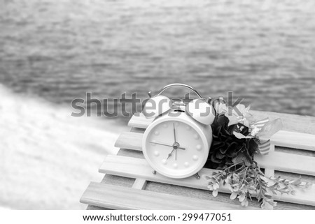 white clock and flower on the table with blur dark beach background ,black and white tone