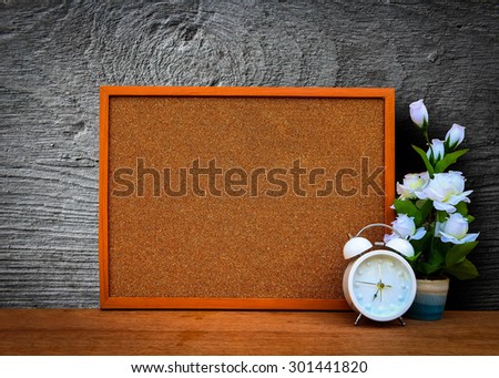blur cork board with white clock and flower vase with grey wooden plate background
