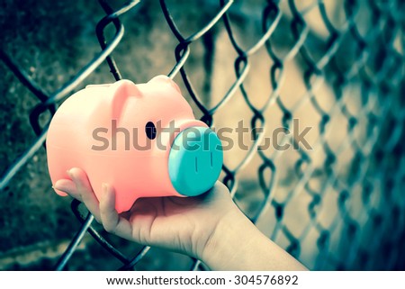 hand holding piggy bank on blur rusty fence background ,green vintage tone