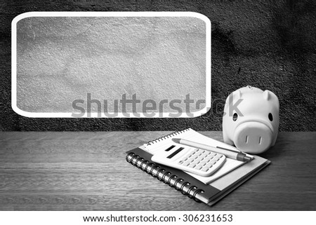 white frame with piggy bank calculator and writing tools on dark crack wall background  ,black and white tone