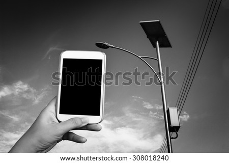 blur hand holding mobile phone  on solar cell street lamp background ,black and white tone