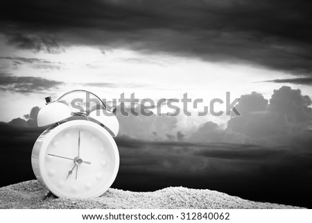 white clock on pink sea sand with blur dark clouds on blue sky background  ,black and white tone