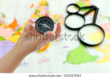 hand holding compass with blur black magnifying glass on map