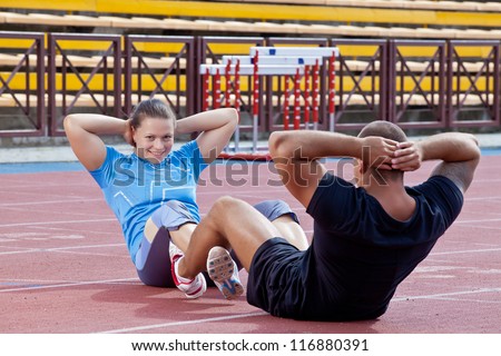 Two athletes help each other to pump the abdominals at the stadium