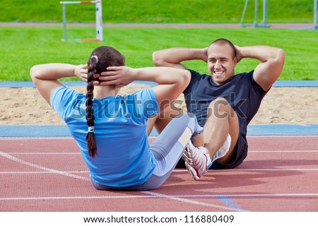 Two athletes help each other to exercise the abdominals at the stadium on a sunny day