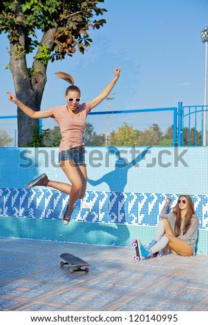 two beautiful young girls in an empty pool, one watches the other making trick on the skateboard