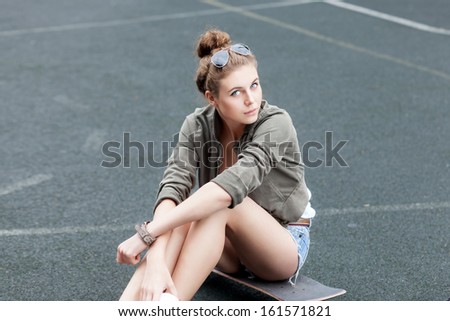 beautiful young girl in jeans shorts sits on skateboard at basketball court